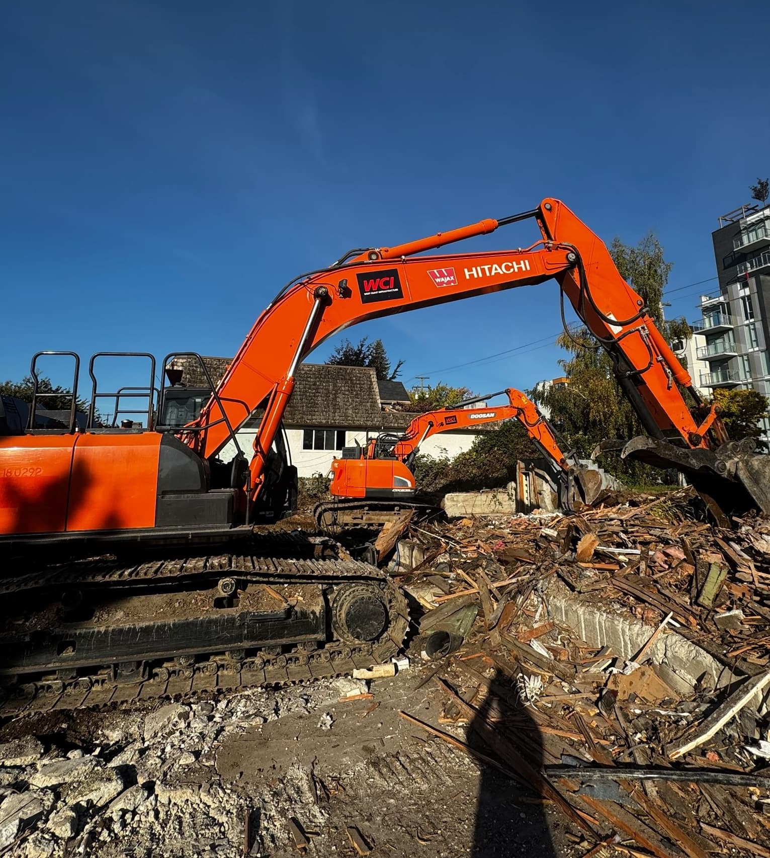 Orange excavator performing demolition work amid debris on an active site.